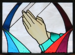 Stained glass window depicting hands folded in prayer